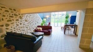 Ein großzügiger Wohnbereich mit Steinwand, einem roten Sofa, einem schwarzen Sofa und einem Essbereich mit Tisch und Stühlen.