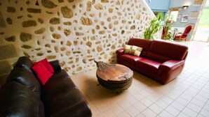 Ein Zimmer mit einer Steinsäule, einem roten Ledersofa, einem Holztisch und einer roten Lederliege.