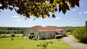 A stone house with a sloped roof, a paved driveway, and a grassy lawn.