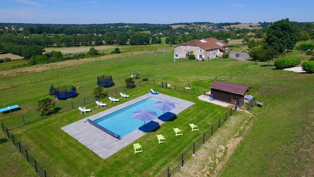 Vista aérea de una propiedad con piscina, sillas de descanso y una casa grande.