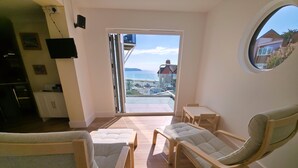 A modern living room with a view of the sea, a dining area, and a kitchen with a TV. - Great dog friendly 2 bed apartment close to village and beach. (Woolacombe)
