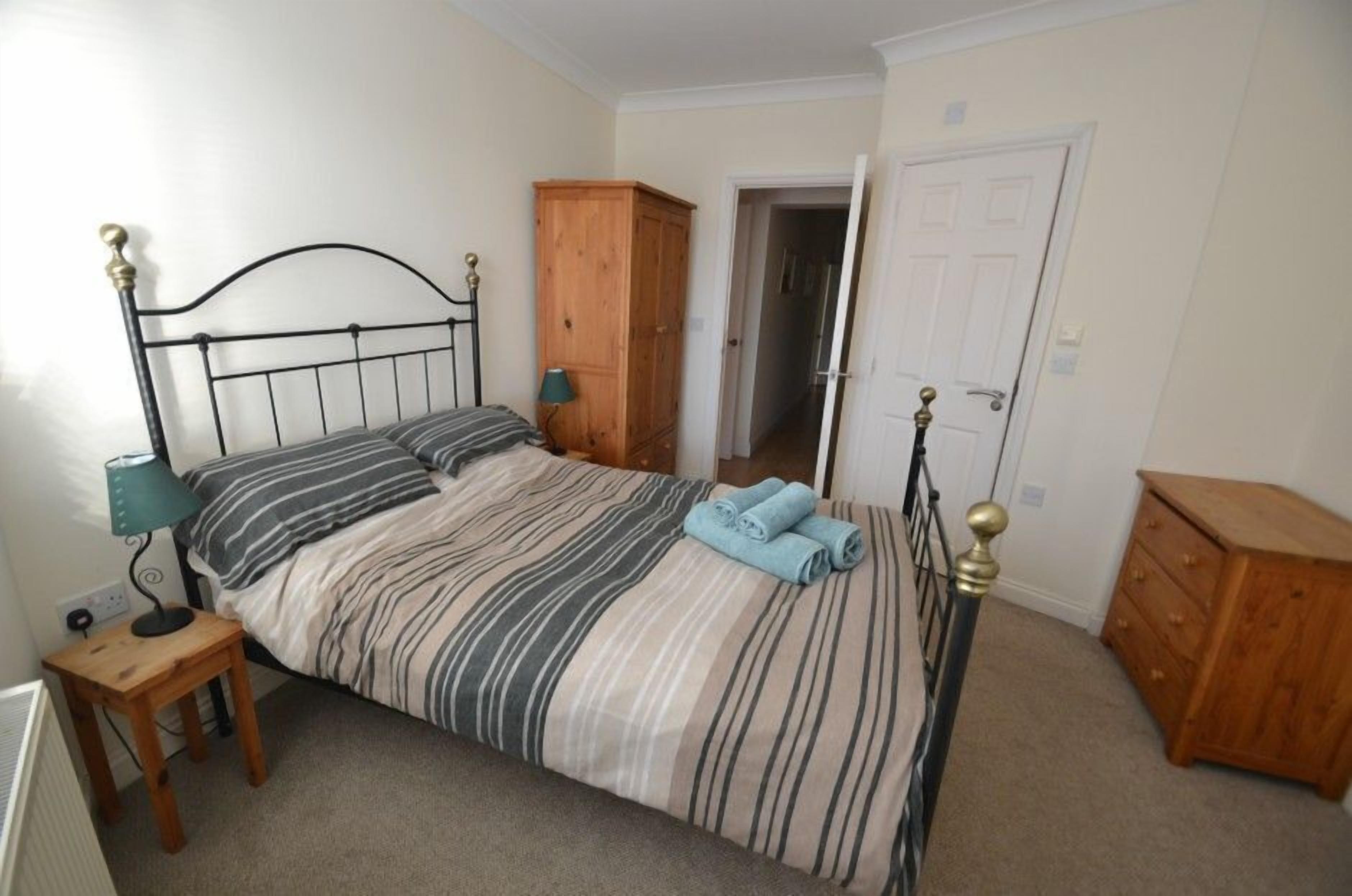 A single bed with a metal frame, a wooden wardrobe, and a small bedside table with a lamp.
