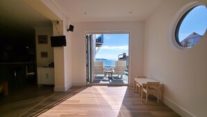 A modern interior with a wooden floor, a dining area with chairs, a TV mounted on the wall, and a view of the sea through a glass door. - Great dog friendly 2 bed apartment close to village and beach. (Woolacombe)