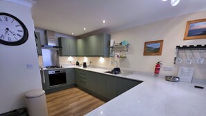 A modern kitchen with a central island, built-in appliances, and a clock on the wall. - Great dog friendly 2 bed apartment close to village and beach. (Woolacombe)