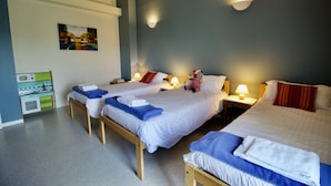 Hotellihuone, jossa on kaksi erillistä sänkyä, pieni työpöytä tuolilla, seinälle asennettu televisio ja lasten leikkialue.