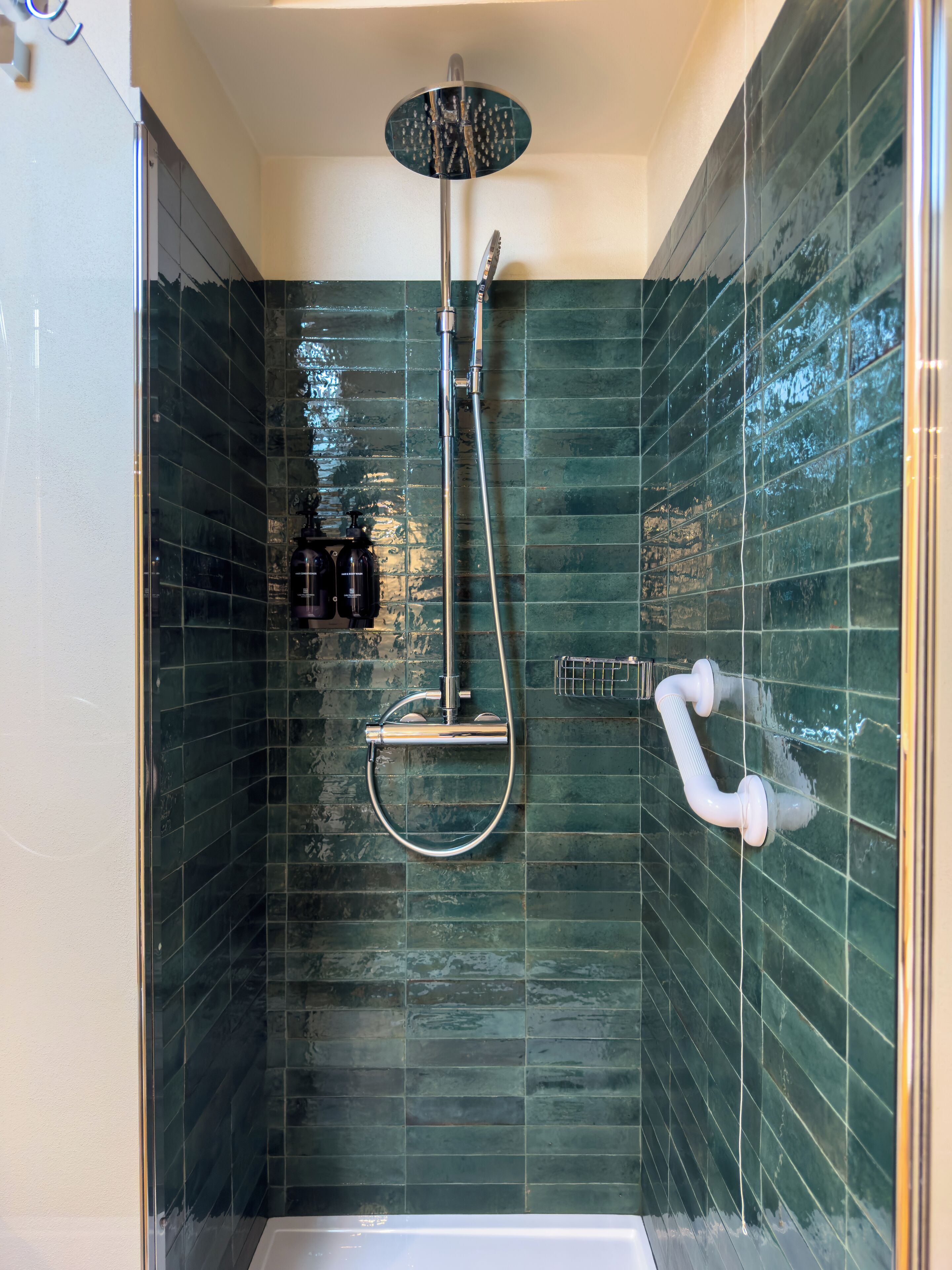 A shower with a handheld showerhead and a wall-mounted faucet, surrounded by green-tiled walls.