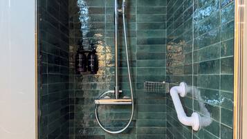 A shower with a handheld showerhead and a wall-mounted faucet, surrounded by green-tiled walls.