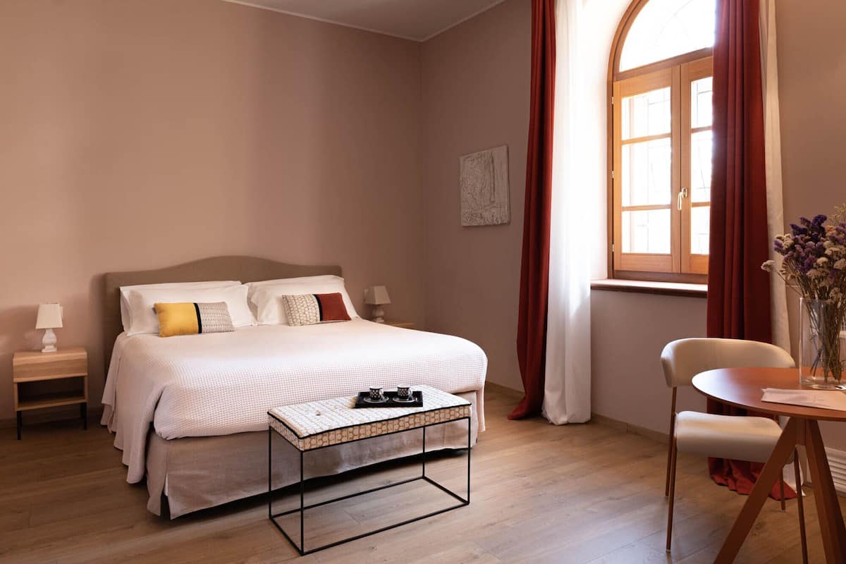 A bedroom with a bed, bedside tables, a small table with a tray, a chair, and a window with curtains.