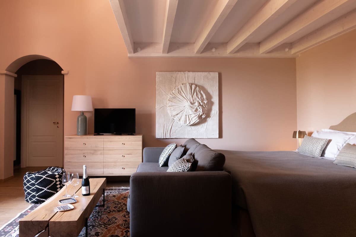 A bedroom with a bed, a TV on a dresser, a sofa, and a decorative wall piece.
