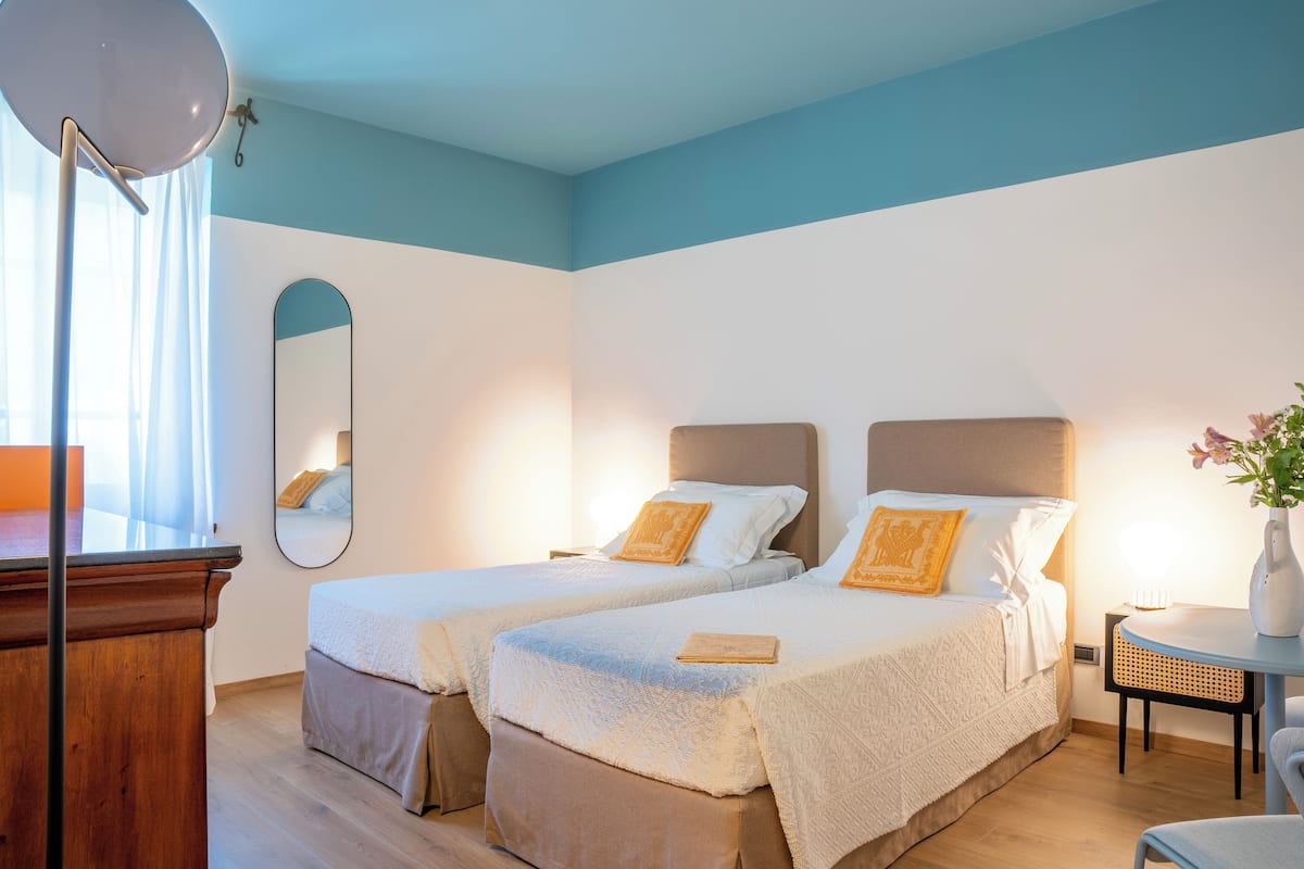A hotel room with two beds, a desk, a chair, a mirror, and a small table with a vase.