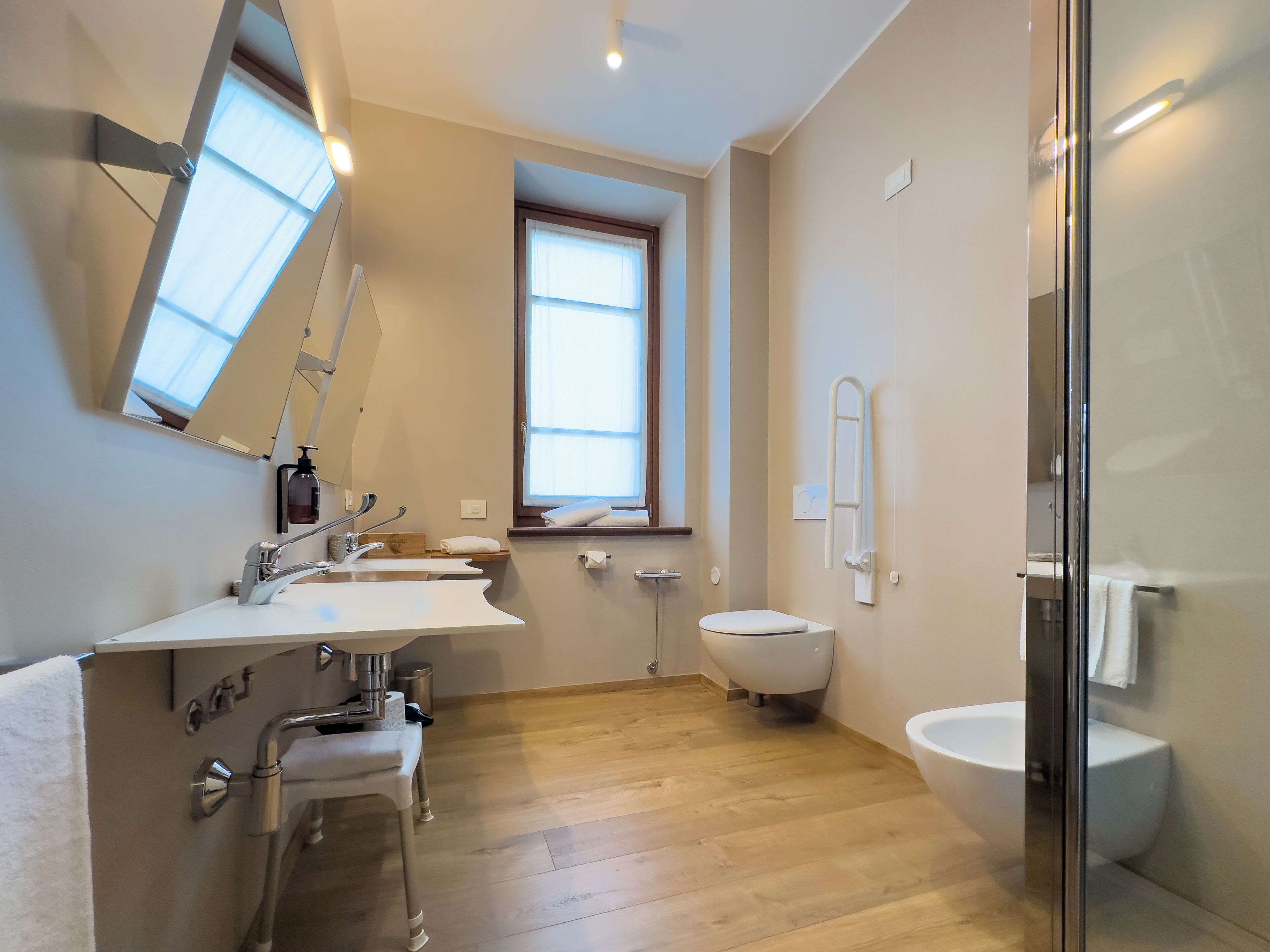 A modern bathroom with a large window, a sink with a mirror, a toilet, and a shower area.