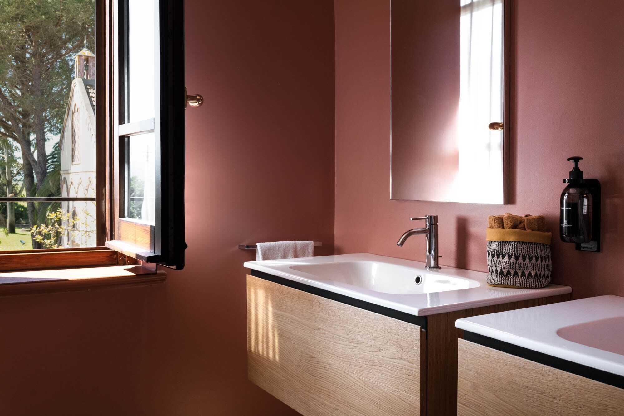 A bathroom with two sinks, a mirror, and a window with a view of trees.