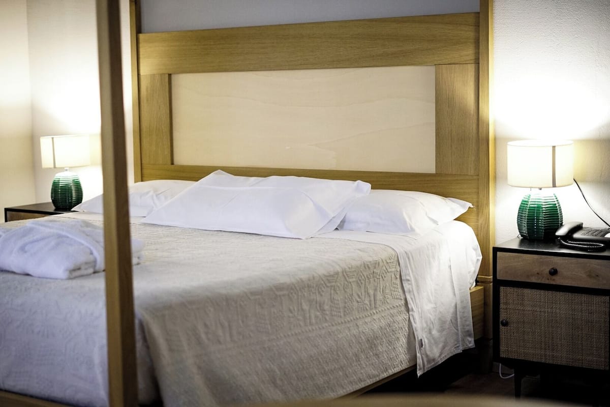 A neatly made bed with white linens, a wooden headboard, and two bedside tables with lamps and a phone.