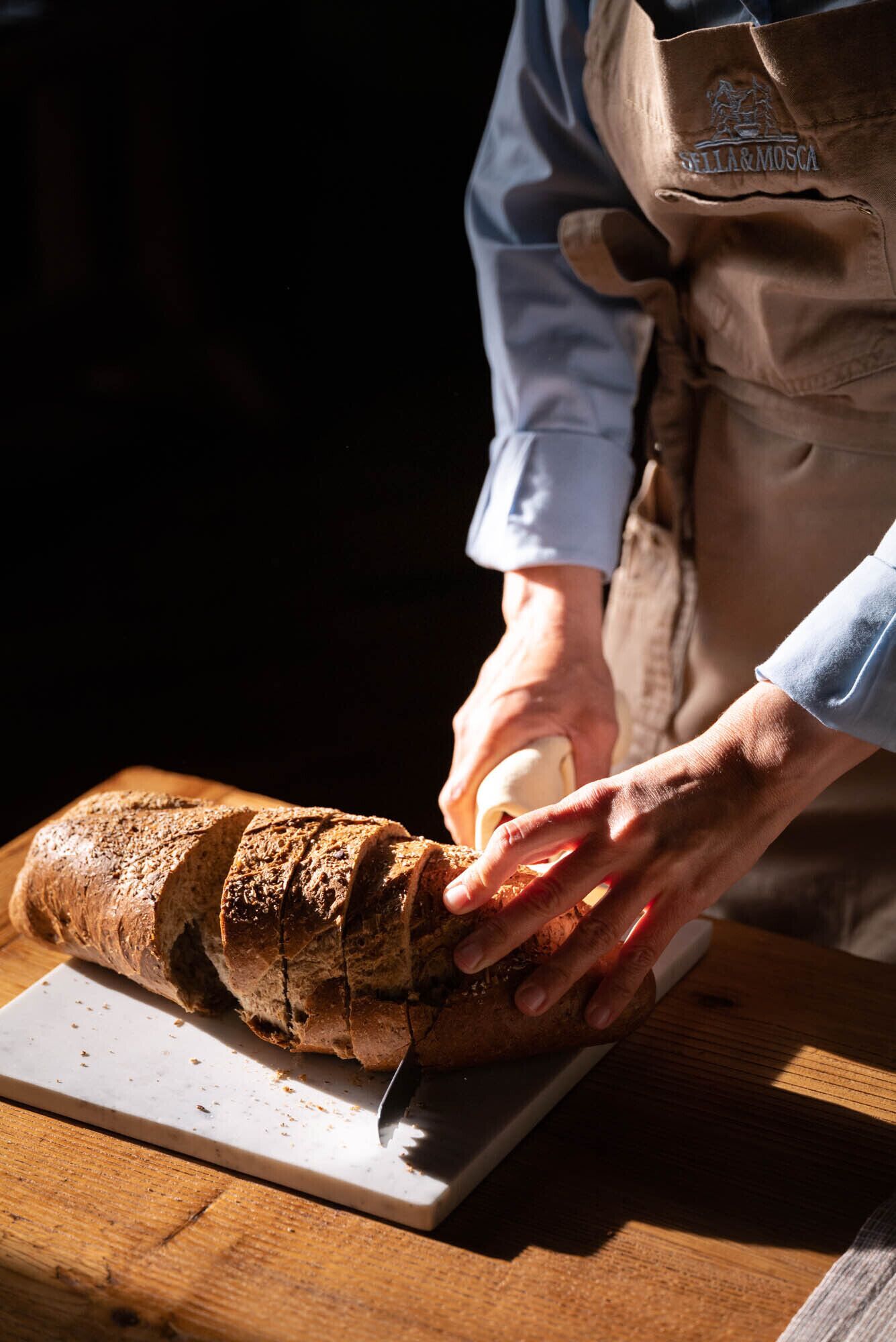 A person slicing a loaf of bread on a wooden cutting board.