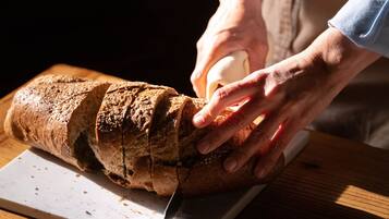A person slicing a loaf of bread on a wooden cutting board.