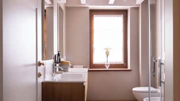 A bathroom with a wooden vanity, a white sink, a glass shower enclosure, and a window with a view of the outdoors.