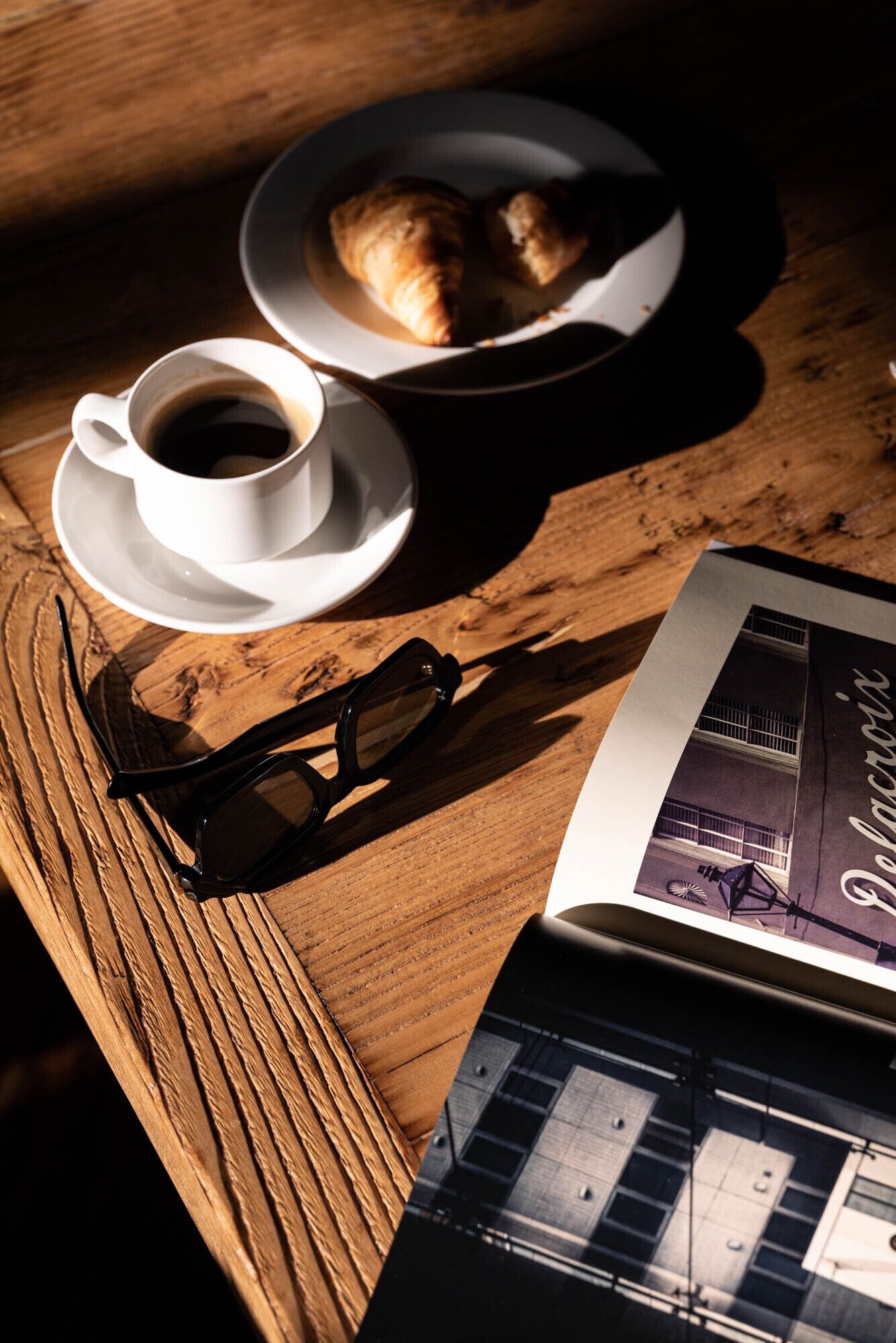 Une table en bois avec une tasse de café, une paire de lunettes de soleil et une brochure.