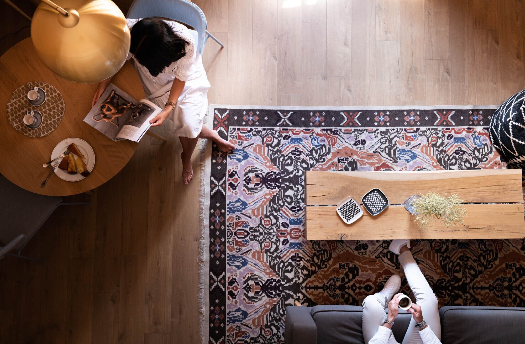 Een kamer met een houten vloer, een kamerbreed tapijt met een patroon, een ronde tafel met een boek, een koffiekop en een decoratief object.