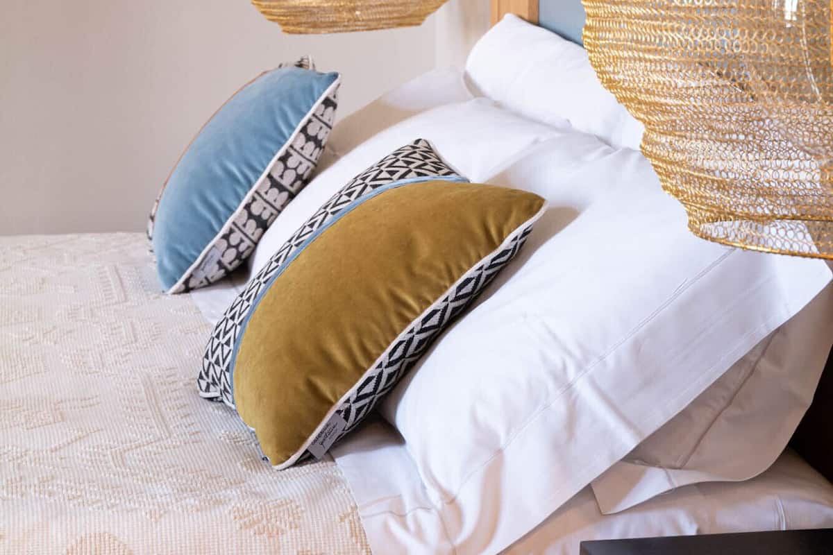 A neatly made bed with patterned pillows and a hanging woven light fixture.