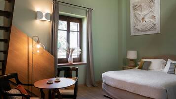 Une chambre à coucher avec un lit, une table sur laquelle sont posées deux tasses, une chaise, une fenêtre avec des rideaux et une lampe fixée au mur.