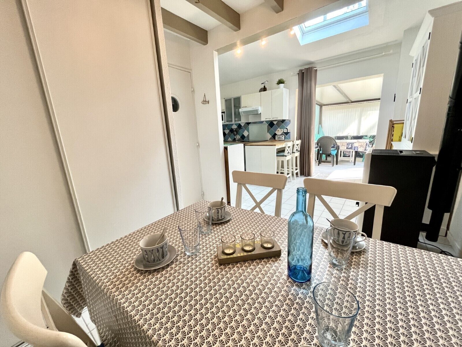 Un coin repas avec une nappe à motifs, des chaises et une cuisine en arrière-plan.
