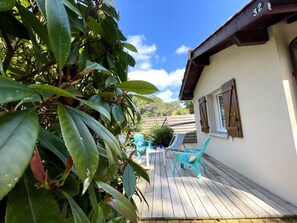 A wooden deck with outdoor furniture, a building with a number '32' sign, and lush greenery. - Maison Jardin du Large by Agence Bru - 323 (Lacanau)