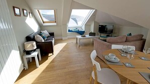 Un salon de style industriel, avec un haut plafond, des fenêtres de toit, un canapé, une table à manger et un téléviseur.