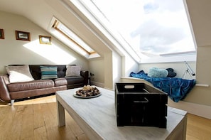 Ein Loft-Zimmer mit geneigter Decke, einem braunen Ledersofa, einem Couchtisch und einem Dachfenster.