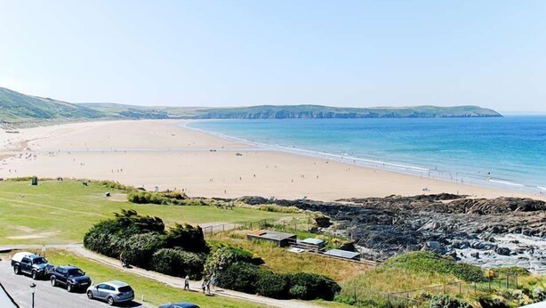 Une plage côtière avec un rivage sablonneux, une mer bleue et limpide, et des falaises rocheuses en arrière-plan.