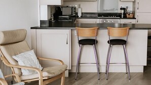 A modern kitchen with white cabinets, a black countertop, stainless steel appliances, and two bar stools. - Cosy 2 bed apartment close to village with 3 balconies and seaviews! (Woolacombe)