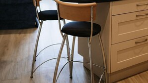 A modern kitchen with a central island, two bar stools, a sofa, and a TV. - Cosy 2 bed apartment close to village with 3 balconies and seaviews! (Woolacombe)