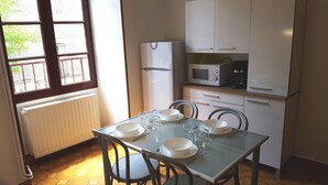A dining area with a table set for four, a refrigerator, a microwave, and a coffee maker. - Studio in the heart of the village (Saint-Jean-du-Bruel)
