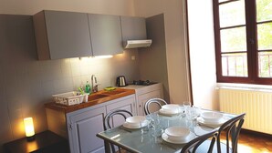 A modern kitchen with grey cabinets, a built-in stove, and a window with a view of trees. - Studio in the heart of the village (Saint-Jean-du-Bruel)