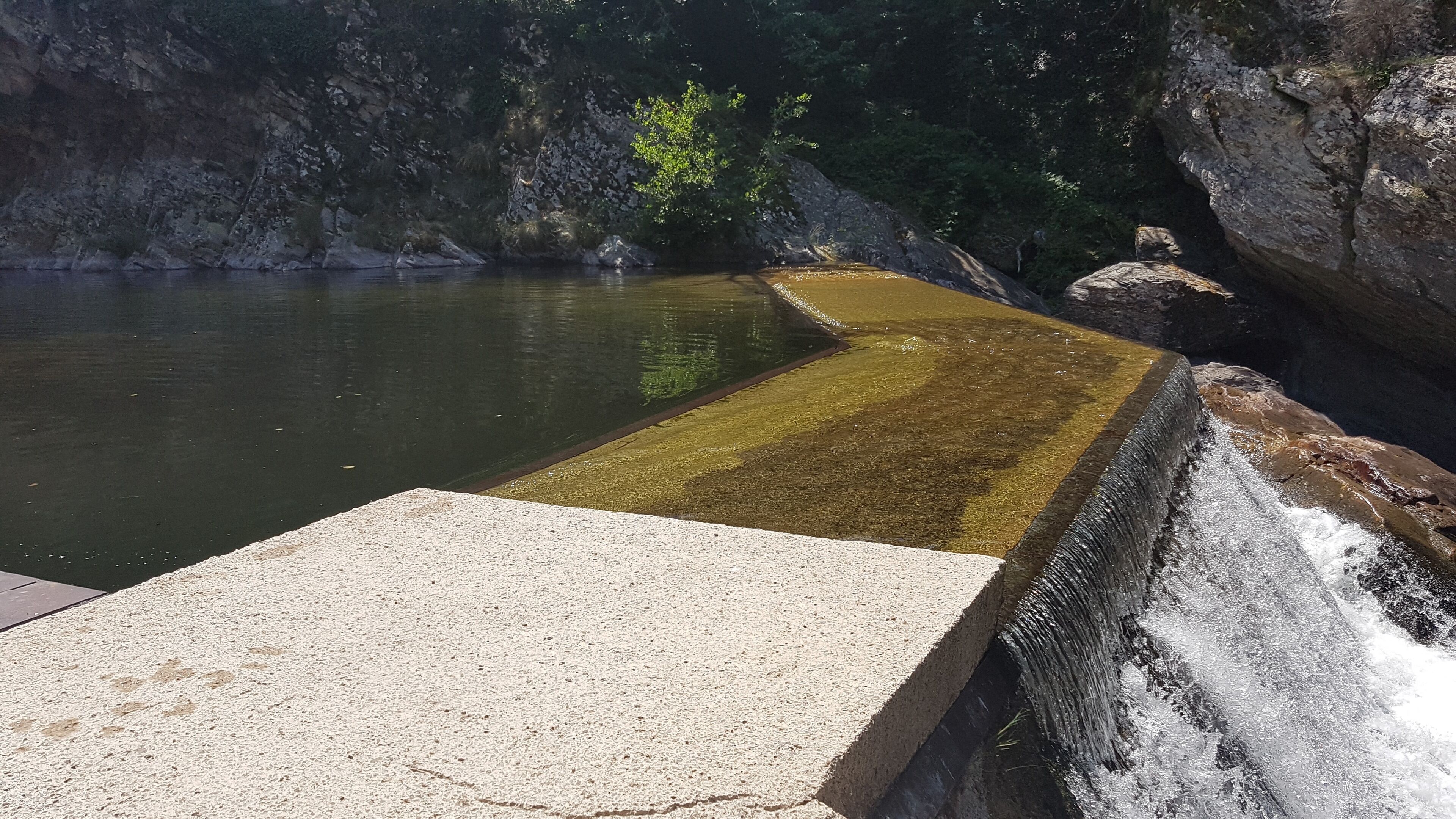 A concrete viewing platform extending over a body of water with a rocky cliff in the background.