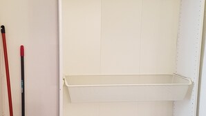 A white closet with wooden hangers, shelves, and a broom. - Studio in the heart of the village (Saint-Jean-du-Bruel)