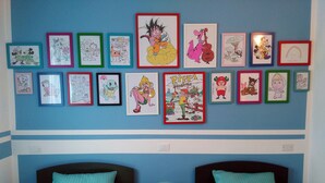 Ein Schlafzimmer mit zwei Betten, beide mit türkisfarbenen Bettbezügen, und einer Wand mit gerahmten Zeichnungen von Zeichentrickfiguren.