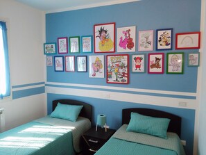 A bedroom with two beds, a blue wall, and various framed pictures.