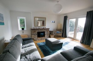 A living room with a stone fireplace, grey sofas, a blue rug, and a balcony with curtains.