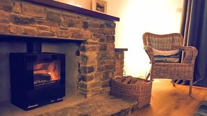 Una chimenea de piedra con un estufa moderna a leña, un sillón de mimbre y una cesta en el suelo.