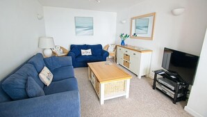A living room with a blue sofa, a wooden coffee table, a TV stand with a flat-screen TV, and a cabinet with wicker baskets.