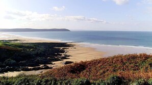 A coastal landscape with a sandy beach, rocky shoreline, and distant hills.