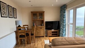 A living room with a sofa, a TV, a wooden cabinet, and a dining table with chairs.
