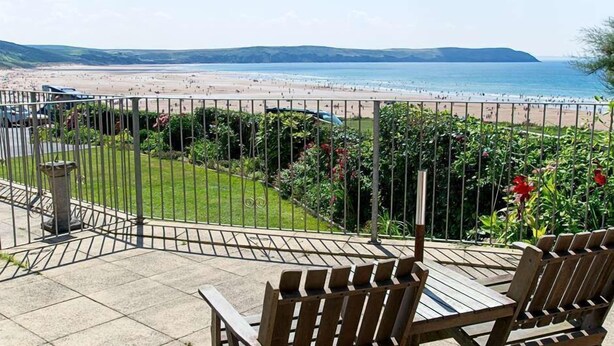 A patio with wooden chairs and a view of a beach.