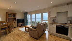 A modern kitchen with white cabinets, a built-in oven, and a dining area with wooden furniture.