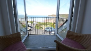 A balcony with a view of the beach and cars parked below.
