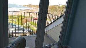 A room with a large sliding glass door leading to a balcony with a view of the beach and cars parked outside.