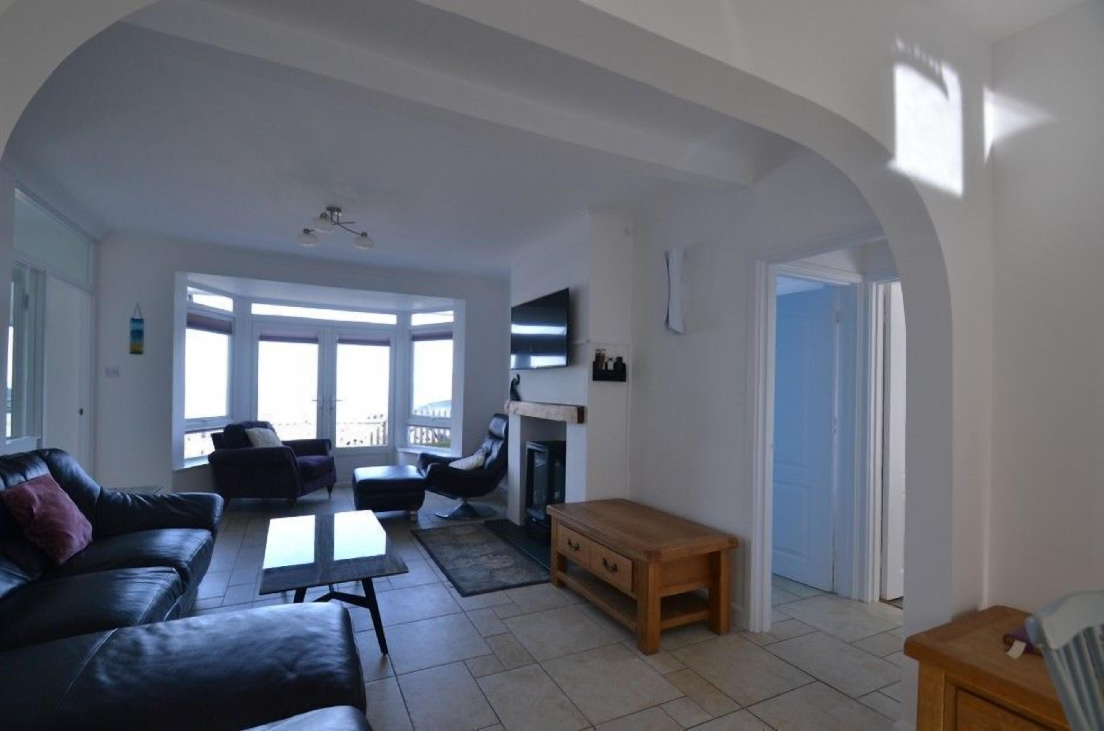 A spacious living room with a fireplace, a sofa, a coffee table, and a TV mounted on the wall.