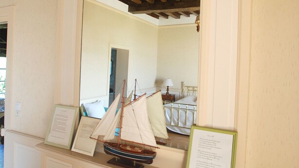 A room with a fireplace, a small sailboat model, and a framed document on the mantel. - -Upper Room- (launay blot)