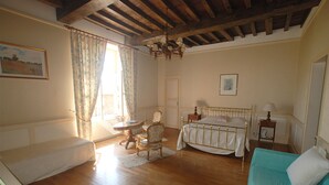 A room with a wooden ceiling, a bed with a white headboard, a blue sofa, a small table, and a chair. - -Upper Room- (launay blot)