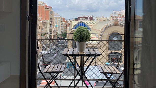 A balcony with a table and chairs, a potted plant, and a view of buildings and a clock tower. - Corsini & Friends a paradise in the center of Tarragona (Tarragona)